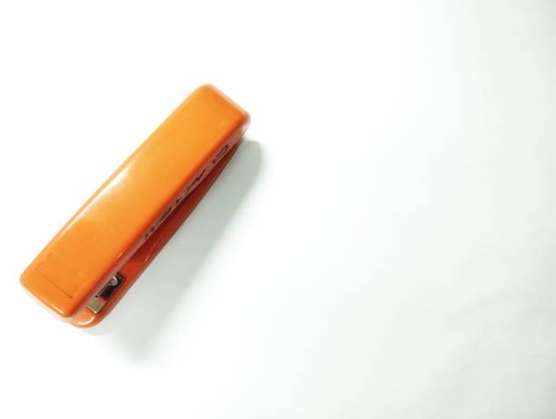 A stapler with a red and white handle sits on a black surface. The stapler is surrounded by a pile of staples