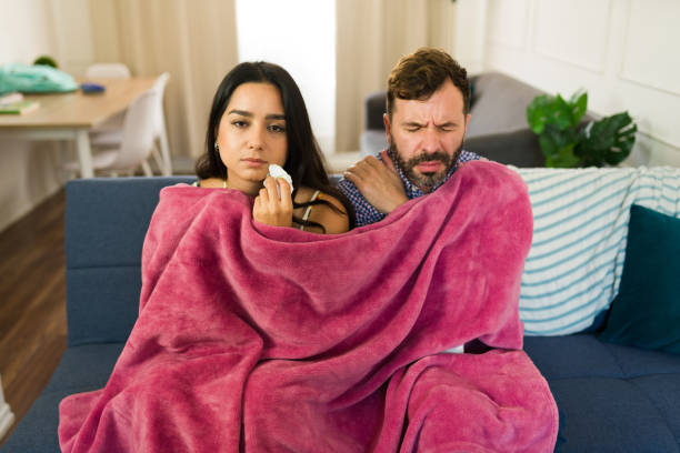 Sick Latin couple snuggled under a blanket while battling a cold or flu at home