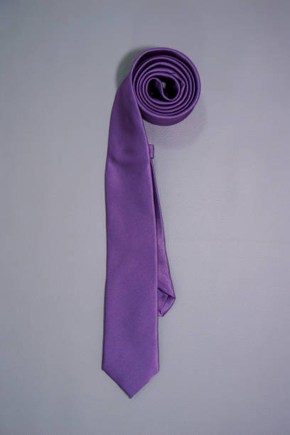 A purple color polyester fabric necktie rolled on dark background close-up view flat lay fashion accessories photography