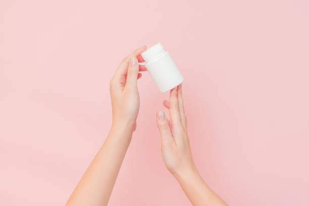 istock View on white bottle plastic tube in hands on pink background. Packaging for pills, capsules, supplements or ointment. Cosmetics 2165811036