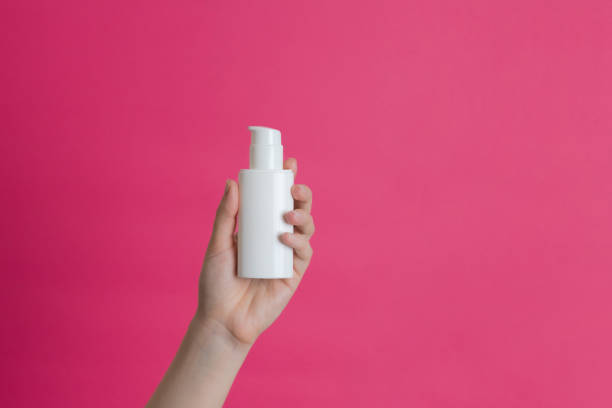 istock White unbranded cream bottle with pump in hand on pink background. Natural moisturizing, nourishing cosmetics for skin, beauty and spa 2165811068