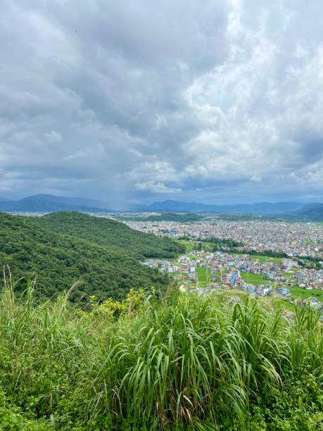 istock City under clouds and green hills. 2165814375