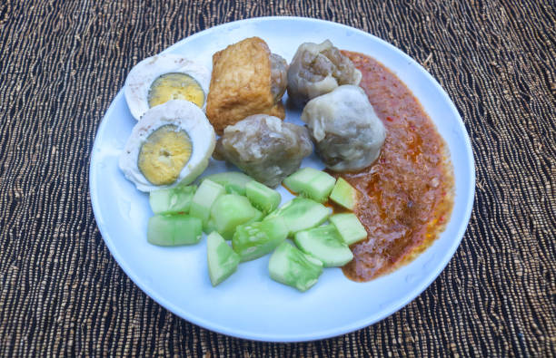 istock Siomay with egg, potato, and cucumber served on a white plate with a table background. Indonesian cuisine Siomay peanut sauce 2165816958