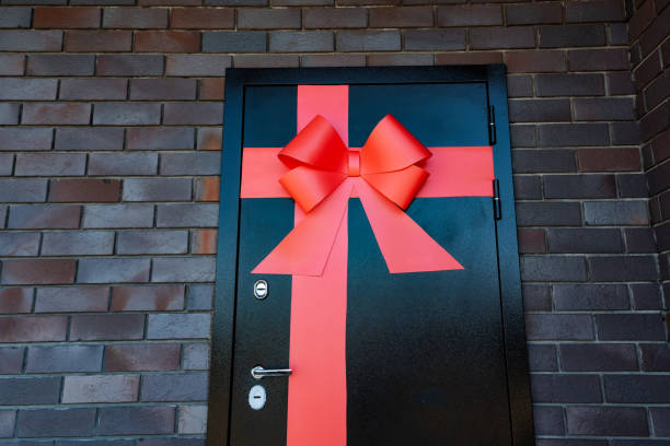 istock I notice a striking black door accented by a vibrant red bow, making it distinct against the brick building. The bold color contrast forms a powerful visual representation 2165820415