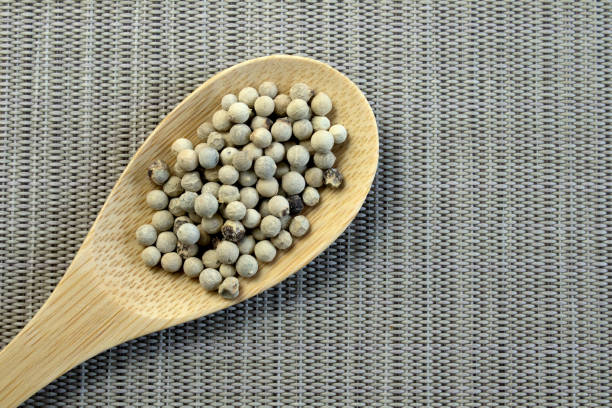 Spices, white peppers, pepper seeds sprinkled on white textured background, close-up top view Narrow focus line, shallow depth of field