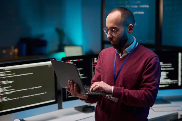 istock Bearded Man Holding Laptop in Cybersecurity Office 2165829873