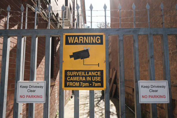 Old yellow metal security camera sign on a spiked metal fence.
