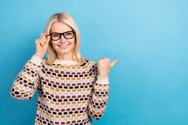 istock Photo of sweet pretty lady dressed pullover arm eyewear pointing thumb empty space isolated blue color background 2165834505
