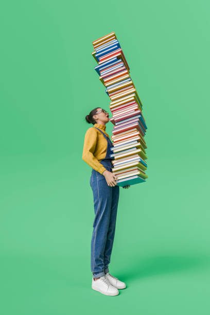 istock Woman Balancing a Tall Stack of Books on Green Background 2165838644