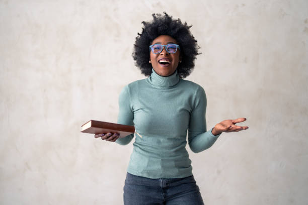 istock Black Woman with Book Laughing Against Grey Background 2165844096