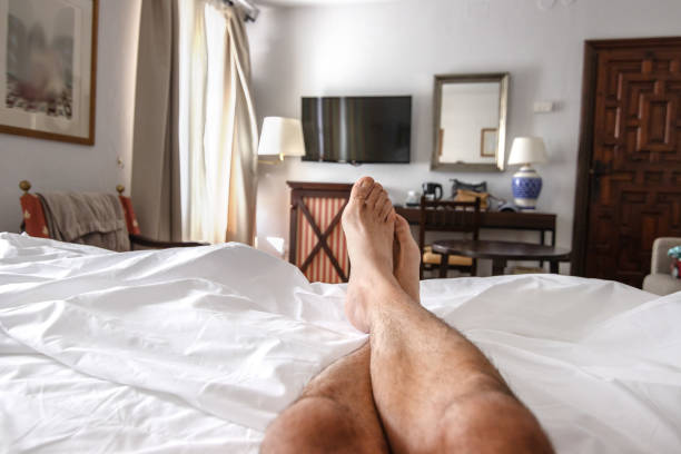 istock A man lying on the bed with white sheets, naked and hairy legs extended. 2165856014