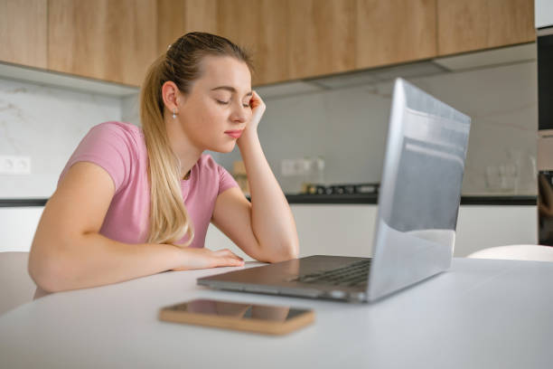 istock Tired woman working remotely from home on a laptop in a kitchen environment 2165857747