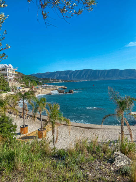 The Albanian pebble beach stretches invitingly along the shoreline, where smooth, round stones create a unique and picturesque landscape. The clear blue sea glistens under the warm sun, its vibrant hues shifting from turquoise to deep azure as it gently laps at the shore. The sound of the waves adds a soothing rhythm, creating a tranquil atmosphere perfect for relaxation. Lush greenery and rocky cliffs frame the beach, enhancing the natural beauty of the scene. This idyllic setting invites visitors to unwind, swim in the refreshing waters, and enjoy the stunning views of the Albanian coast.