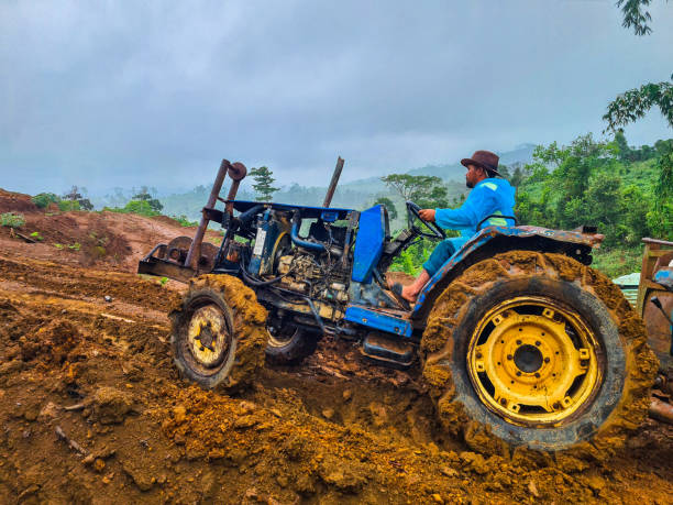 High-quality image of a farmer driving a tractor through a muddy field on a farm during rainy weather. The photo captures the challenging conditions and the hard work involved in agricultural activities, with rain and mud adding to the atmosphere. Ideal for illustrating the realities of farming, rural life, and weather impacts on agriculture