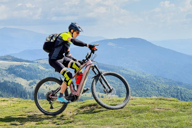 Cyclist man riding electric mountain bike outdoors along grassy trail in the mountains. stock photo