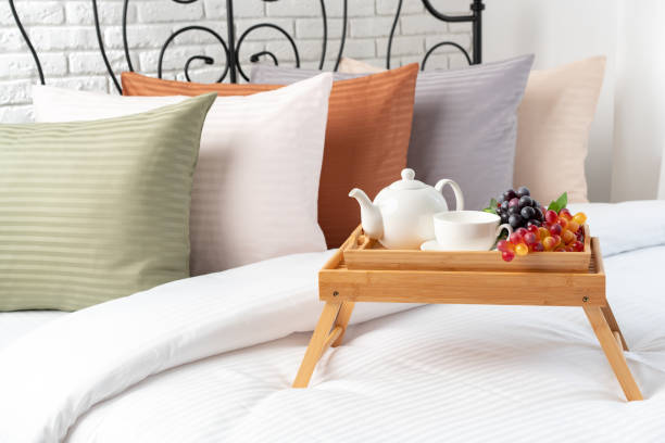 A tray with hot tea, cookies, apple and winter decoration placed on cozy bed.