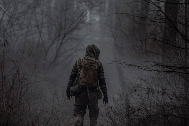 A man in camouflage in a post-apocalyptic, smoky, dark forest. Back view.