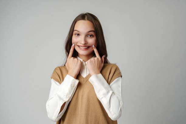 istock Young Woman Smiling and Touching Cheeks With Fingers Against Grey Background 2165871721