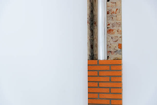 Beautiful minimalist view of an unfinished brick fireplace chimney with a metal pipe inside, to the right between white walls with copy space to the left in a room during the day, side view close up. Clean brickwork concept.