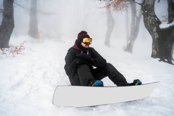 Young man leaning a snowboard and gesturing thumbs up isolated on white background