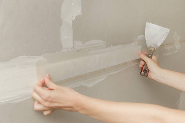 istock Woman taping and mudding joins pieces of drywall into a single solid wall. Fixing dry wall surface and preparation for painting. DIY housing improvement project. 2165878972