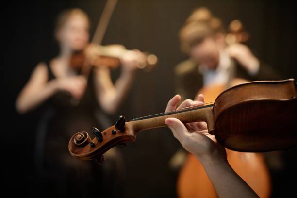 Classical Music Artist Playing Violin in String Quartet Close up on hand of unrecognizable female string ensemble musician playing on violin moving fingers on fretboard on blurred background, focus on hand, copy space string ensemble stock pictures, royalty-free photos & images