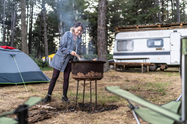 A young woman makes a fire for preparing meal in nature while camping in the forest