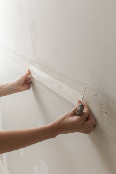 istock Woman taping and mudding joins pieces of drywall into a single solid wall. Fixing dry wall surface and preparation for painting. DIY housing improvement project. 2165879291