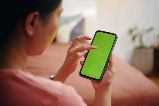 istock Holding Smartphone with Blank Green Screen Indoors 2165889098