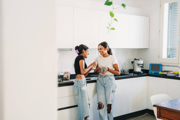 istock Two smiling sisters drinking coffee together in a modern kitchen 2165889592