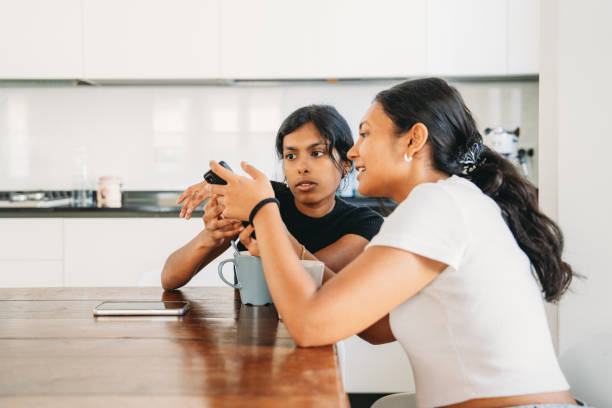 istock Two young women using smartphone and talking in a kitchen 2165889600