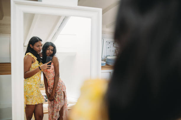 Two young women wearing summer dresses are taking a selfie in a bright interior with a smartphone