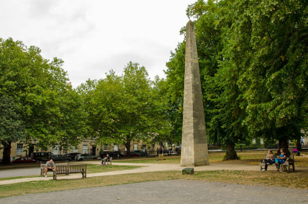 September 3, 2022: people resting on the benches surrounding the historic obelisk in Queen's Square in the centre of the city of Bath, Somerset on a late summer afternoon.