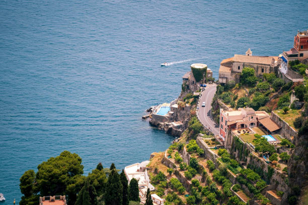 A breathtaking view of a coastal road winding along cliffs with villas and the deep blue ocean in the background.