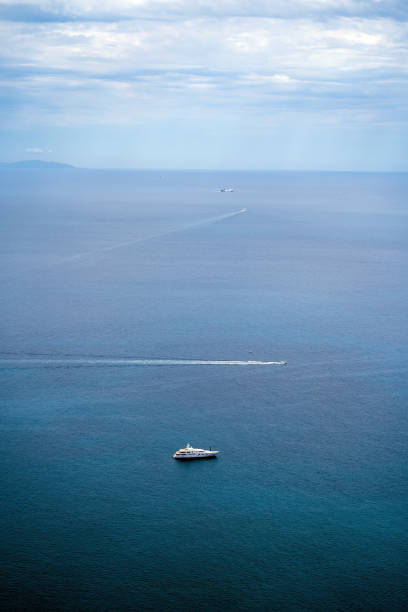 A serene ocean scene featuring multiple boats against a backdrop of calm blue waters and a partly cloudy sky.