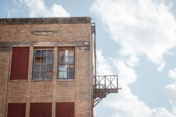 An old brick building with boarded windows and a fire escape against a cloudy sky