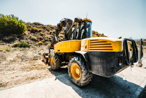 A yellow construction vehicle with a large bucket on the back. The vehicle is parked in a grassy area next to a road