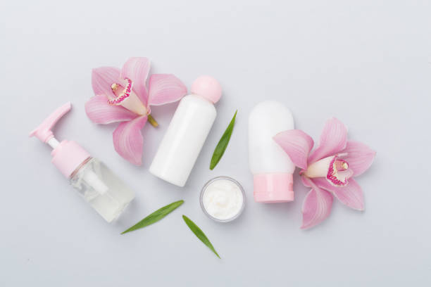 istock Bottles and jars with cream and orchids on color background, top view 2165908472