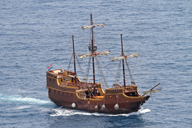 A small wooden boat with a white sail is on a black background. The boat is the main focus of the image, and it is a model or a toy. The black background emphasizes the boat's size