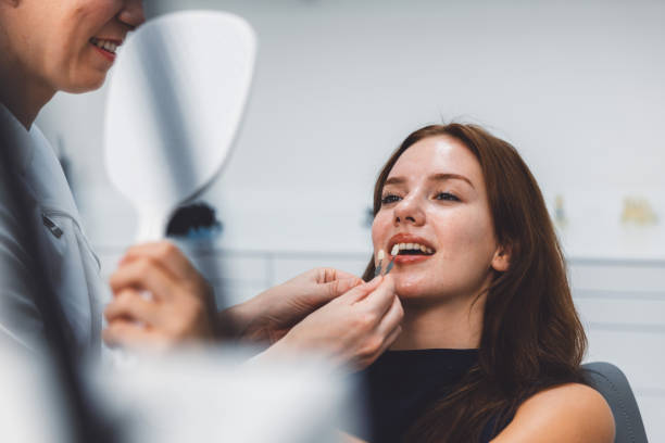 Patient Getting Dental Veneer Fitted A dental professional is fitting a dental veneer on a smiling patient in a modern dental clinic. The patient looks pleased as she examines her smile in a handheld mirror. cosmetic dentistry stock pictures, royalty-free photos & images