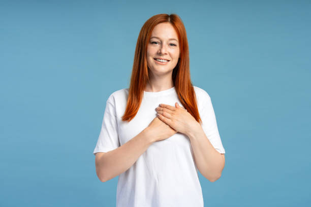 Grateful woman holding hands on chest smiling on blue background looking at camera