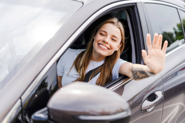 Happy young woman driver waving from car window