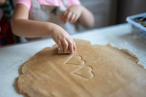 Family Christmas cooking tradition. Little girl hands cutting heart shaped gingerbread cookies from pastry dough.