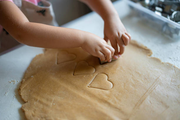 Family Christmas cooking tradition. Little girl hands cutting heart shaped gingerbread cookies from pastry dough.