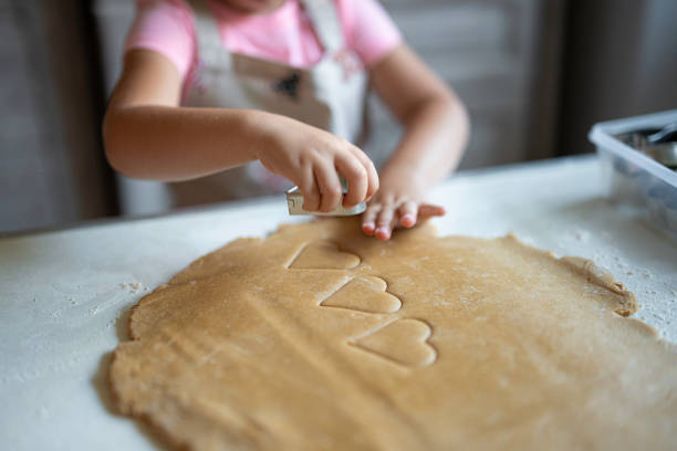 Family Christmas cooking tradition. Little girl hands cutting heart shaped gingerbread cookies from pastry dough.