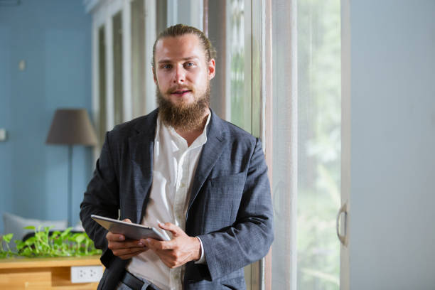 istock Portrait handsome businessman with beard holding tablet standing at side window office. happy smart man mature wear suit. 2165959627