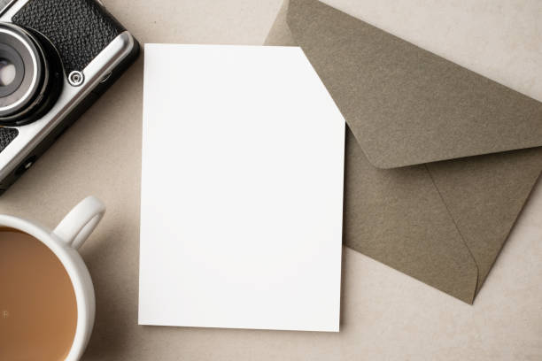 istock White blank greeting or invitation card and envelope with coffee cup, notebook and pencil on beige background. Mockup presentation. Flat lay. 2165962277
