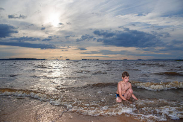 A boy plays in the water on the shore of a lake.