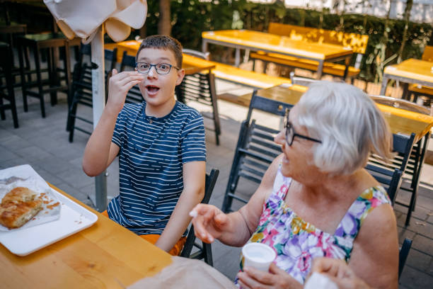Teenager having breakfast together with grandparents sitting in front of bakery and having fun