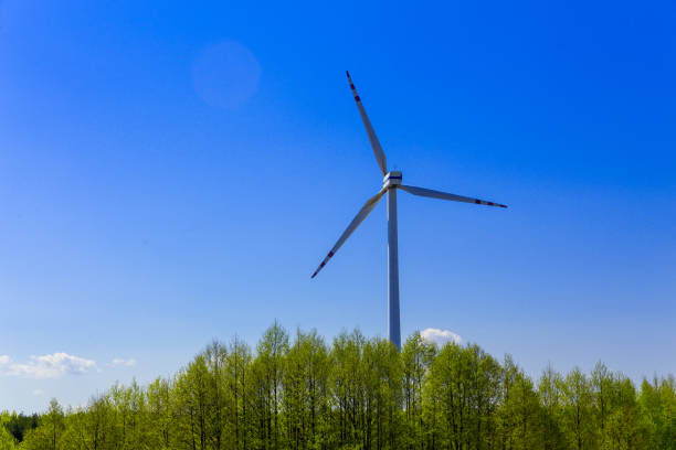 Wind turbines in the European forest. Windmill on a colorful landscape with trees and field. Green renewable electricity banner.